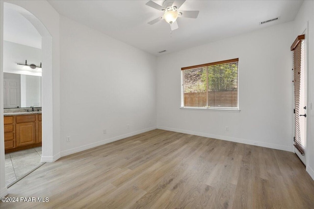 unfurnished bedroom featuring ceiling fan, sink, ensuite bathroom, and light hardwood / wood-style flooring