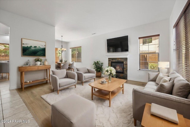 living room with a stone fireplace, plenty of natural light, light hardwood / wood-style floors, and a notable chandelier