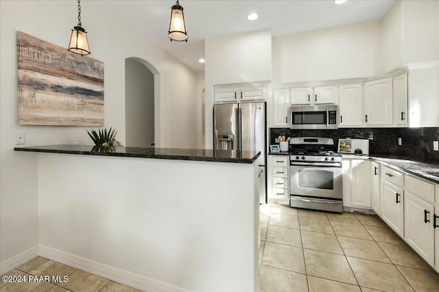 kitchen featuring appliances with stainless steel finishes, tasteful backsplash, dark stone countertops, white cabinetry, and hanging light fixtures