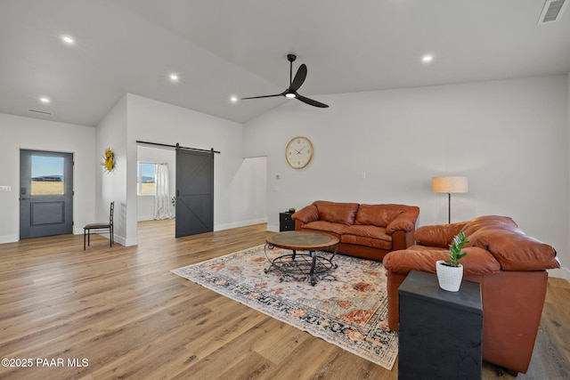 living room with ceiling fan, lofted ceiling, a barn door, and light hardwood / wood-style flooring