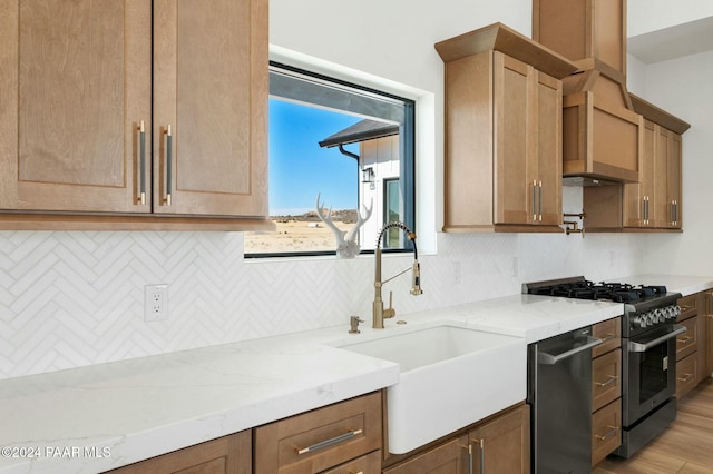 kitchen with light stone countertops, sink, tasteful backsplash, appliances with stainless steel finishes, and light wood-type flooring