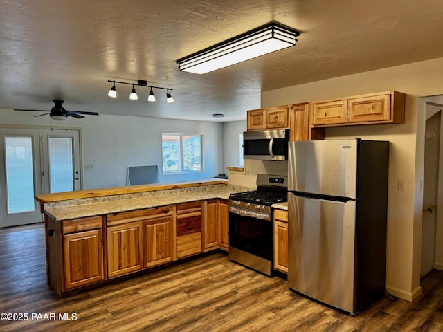 kitchen with kitchen peninsula, stainless steel appliances, light stone counters, a textured ceiling, and hardwood / wood-style floors