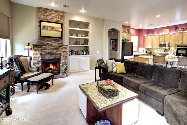 living room featuring a stone fireplace, light carpet, and built in features