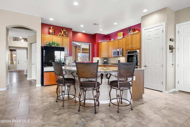 kitchen with a kitchen island, a breakfast bar, tasteful backsplash, light stone counters, and stainless steel appliances