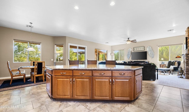 kitchen with decorative light fixtures, light stone countertops, ceiling fan, and a kitchen island