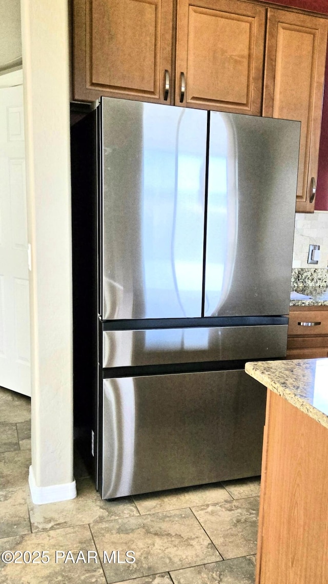 kitchen with stainless steel refrigerator, decorative backsplash, and light stone counters