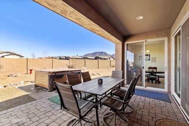 view of patio / terrace featuring a fenced backyard, a mountain view, a hot tub, and outdoor dining space