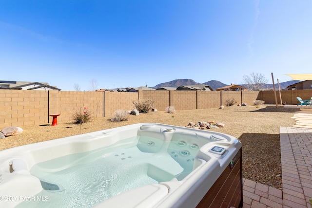 view of swimming pool with a fenced backyard, a mountain view, and a hot tub