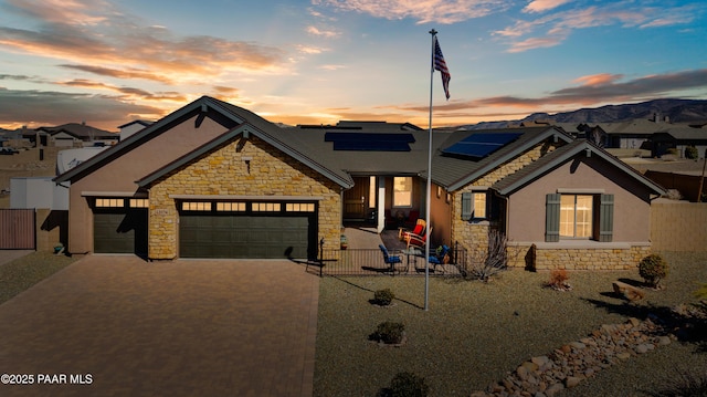 view of front of property with driveway, stone siding, stucco siding, solar panels, and a garage