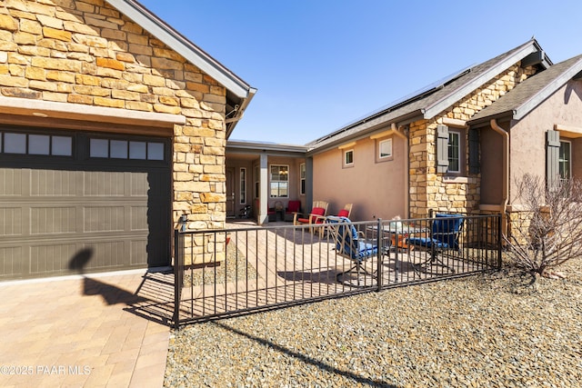 view of side of property featuring stone siding, stucco siding, fence, solar panels, and a garage