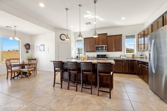 kitchen with dark brown cabinetry, appliances with stainless steel finishes, light tile patterned floors, a kitchen island with sink, and visible vents