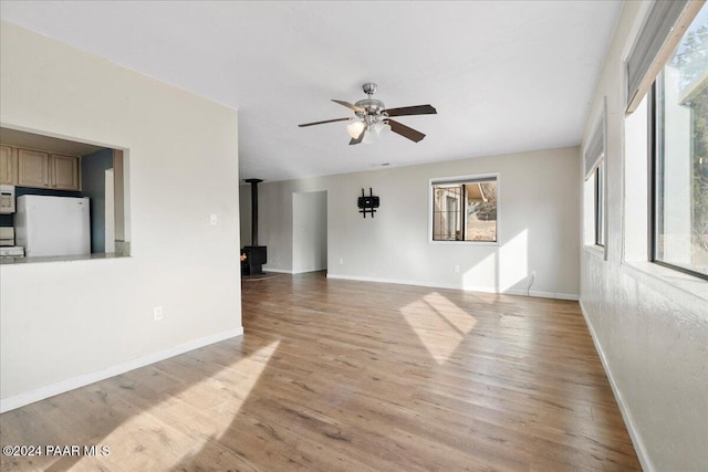 empty room featuring ceiling fan, light hardwood / wood-style flooring, and a wood stove