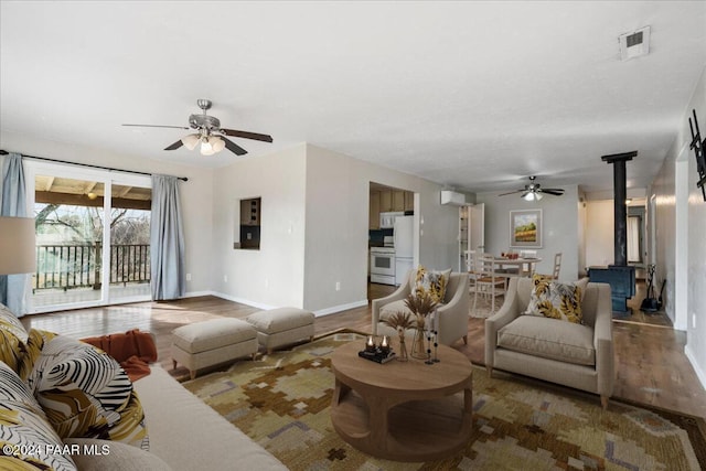 living room featuring ceiling fan, a wood stove, and dark wood-type flooring