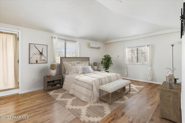 bedroom featuring light wood-type flooring, vaulted ceiling, and a wall mounted air conditioner