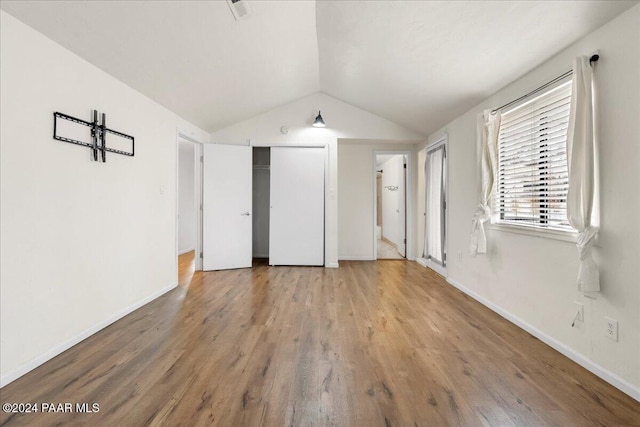 unfurnished bedroom with hardwood / wood-style floors, vaulted ceiling, and a closet