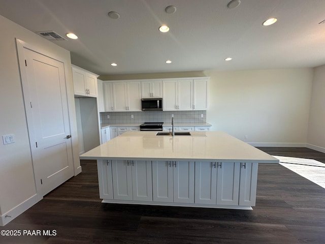 kitchen featuring dark wood-type flooring, a sink, white cabinetry, appliances with stainless steel finishes, and an island with sink