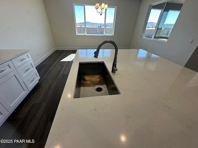 kitchen featuring dark wood finished floors, a notable chandelier, white cabinetry, a sink, and baseboards