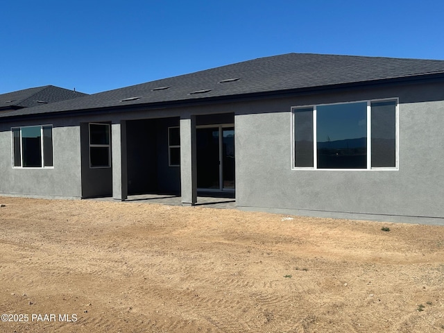 back of house featuring stucco siding and roof with shingles