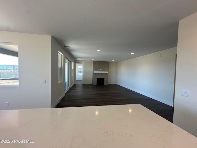 unfurnished living room featuring a large fireplace, baseboards, dark wood-style floors, and recessed lighting