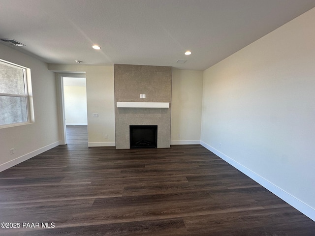 unfurnished living room featuring a large fireplace, baseboards, dark wood-style floors, and visible vents