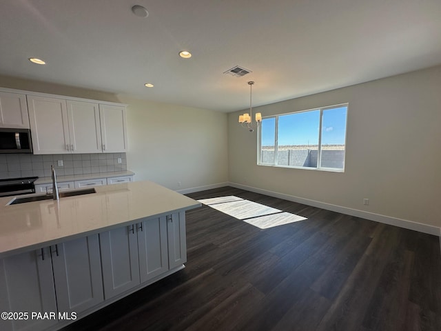 kitchen with dark wood-style floors, stainless steel microwave, visible vents, backsplash, and a sink