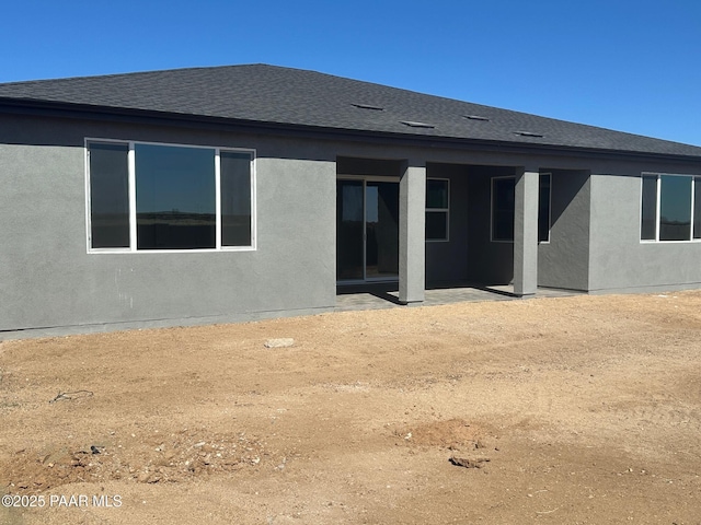 back of property with roof with shingles, a patio area, and stucco siding