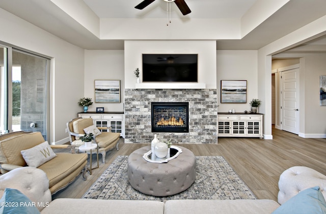 living room with ceiling fan, wood-type flooring, a tile fireplace, and a tray ceiling