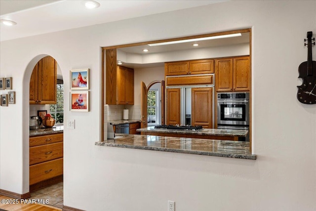1167 Eagles Nest, Prescott, AZ 86303 - kitchen featuring arched walkways, appliances with stainless steel finishes, brown cabinets, decorative backsplash, and recessed lighting