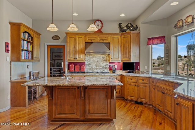 kitchen featuring hanging light fixtures, a sink, an island with sink, light stone countertops, and wall chimney exhaust hood