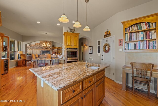 kitchen with arched walkways, a sink, an island with sink, and light stone countertops