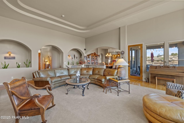 living area featuring a chandelier, arched walkways, a high ceiling, and a tray ceiling