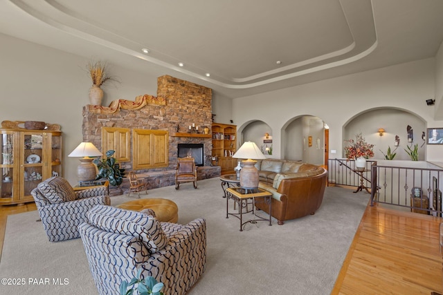 living area with arched walkways, a high ceiling, a tray ceiling, light wood-style floors, and a fireplace