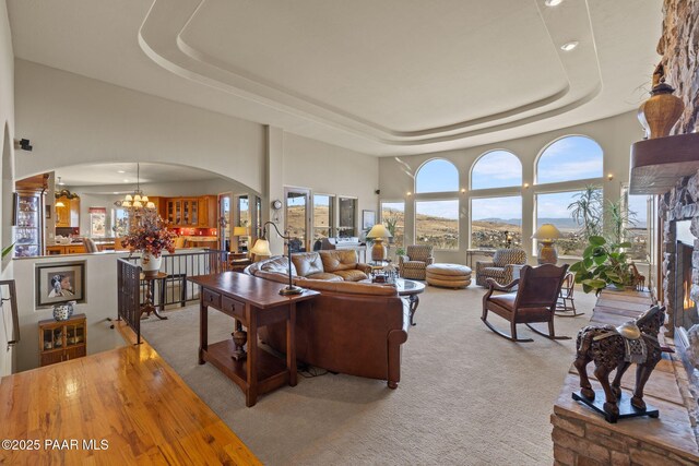 living area featuring a tray ceiling, arched walkways, a glass covered fireplace, and light colored carpet