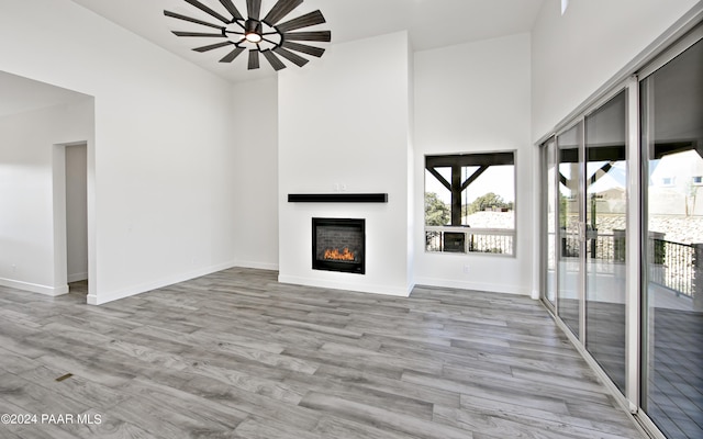 12290 N Thrine Cir, Prescott, AZ 86305 - unfurnished living room with a towering ceiling, baseboards, a lit fireplace, and wood finished floors