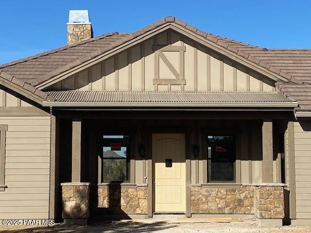 view of front of house featuring covered porch, stone siding, board and batten siding, and a tile roof