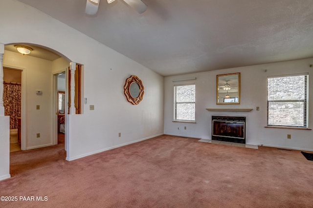 unfurnished living room with a fireplace with flush hearth, a ceiling fan, arched walkways, and carpet floors