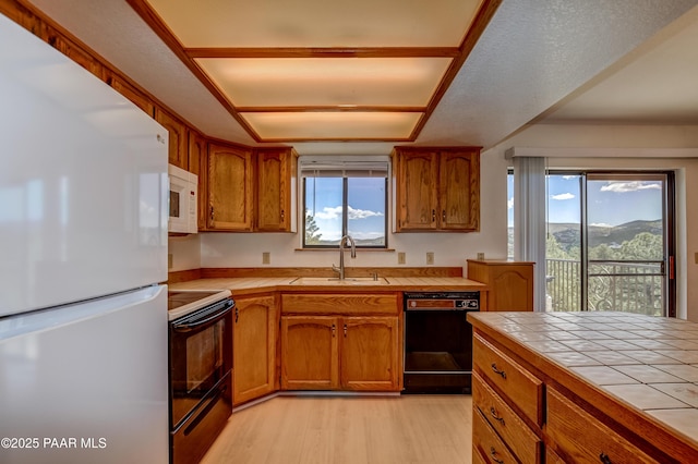 kitchen featuring white appliances, tile counters, brown cabinetry, and a sink