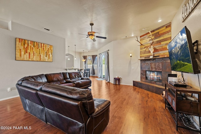 living room with ceiling fan, wood-type flooring, and a tile fireplace