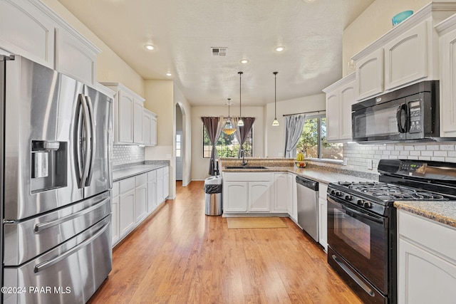 kitchen with pendant lighting, black appliances, white cabinets, decorative backsplash, and light hardwood / wood-style floors