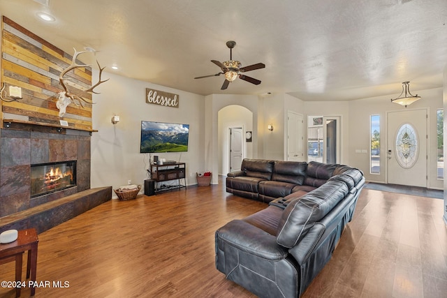 living room featuring a stone fireplace, ceiling fan, and dark hardwood / wood-style flooring