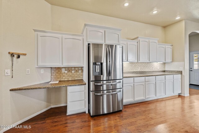 kitchen with backsplash, white cabinetry, wood-type flooring, and stainless steel refrigerator with ice dispenser