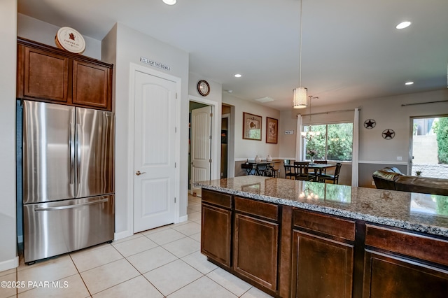 kitchen featuring pendant lighting, light tile patterned floors, freestanding refrigerator, stone counters, and recessed lighting