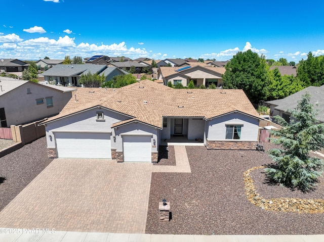 ranch-style house featuring a residential view, decorative driveway, an attached garage, stone siding, and stucco siding