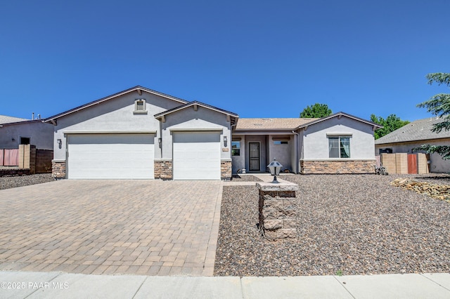 single story home featuring decorative driveway, a garage, stone siding, and stucco siding