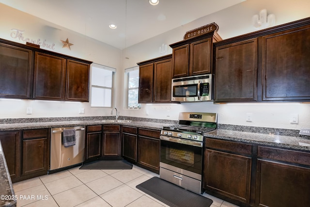 kitchen with dark stone counters, stainless steel appliances, light tile patterned flooring, and a sink