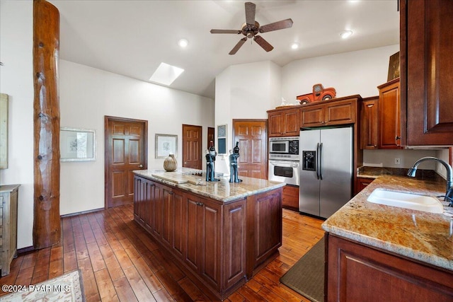 kitchen featuring a center island, sink, a skylight, appliances with stainless steel finishes, and light stone counters