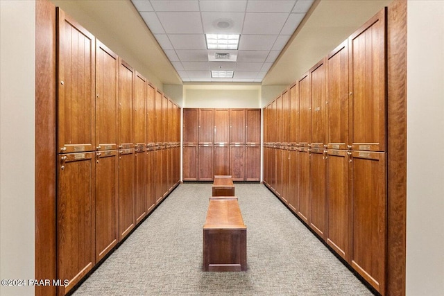 corridor featuring a paneled ceiling, light colored carpet, and wood walls