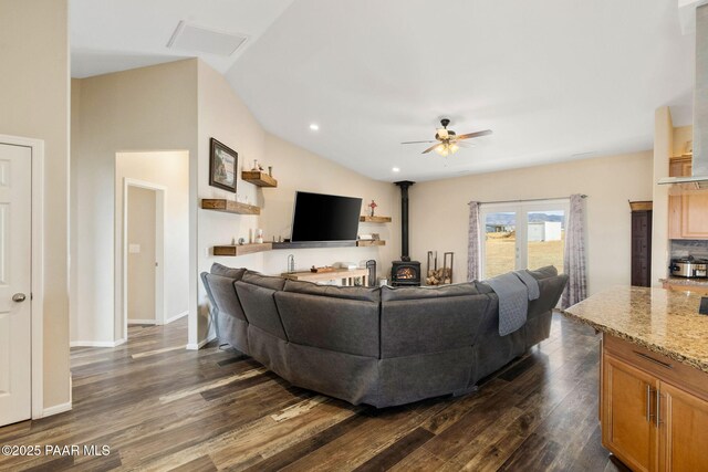 living room featuring a wood stove, ceiling fan, dark wood-type flooring, and vaulted ceiling