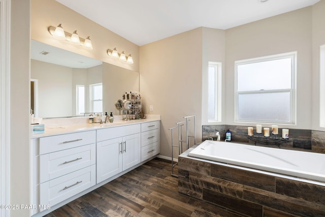 bathroom featuring hardwood / wood-style floors, a relaxing tiled tub, and vanity