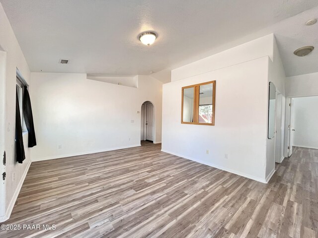 spare room featuring arched walkways, lofted ceiling, visible vents, baseboards, and light wood-style floors